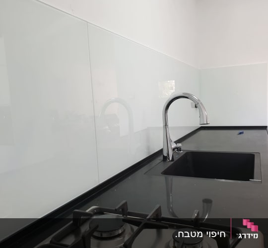 זכוכית שקופה על קיר מטבח מעל כיור וברז